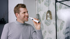 Man using whitening electric toothbrush replacement head on white Jordan electric toothbrush in bathroom mirror