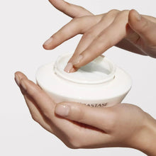 Hands holding open hair mask jar with thick white cream