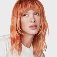 Kerastase refillable hair oil showcased on a model with vibrant orange hair for a healthy shine