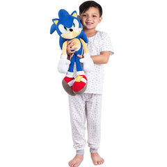 Child holding a blue kids sonic plush pillow toy wearing white pajamas with small patterns