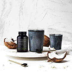 Kiki Health activated charcoal UAE jar with two charcoal coconut smoothies and broken coconuts