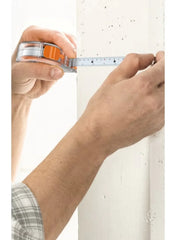Hands measuring a wall edge with a tape measure