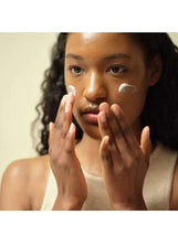 Woman applying white facial moisturizer to her cheek with her fingertips