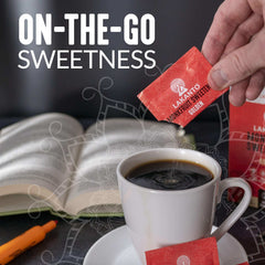 Lakanto monkfruit sweetener packets being poured into a cup of black coffee from a red packet near an open book
