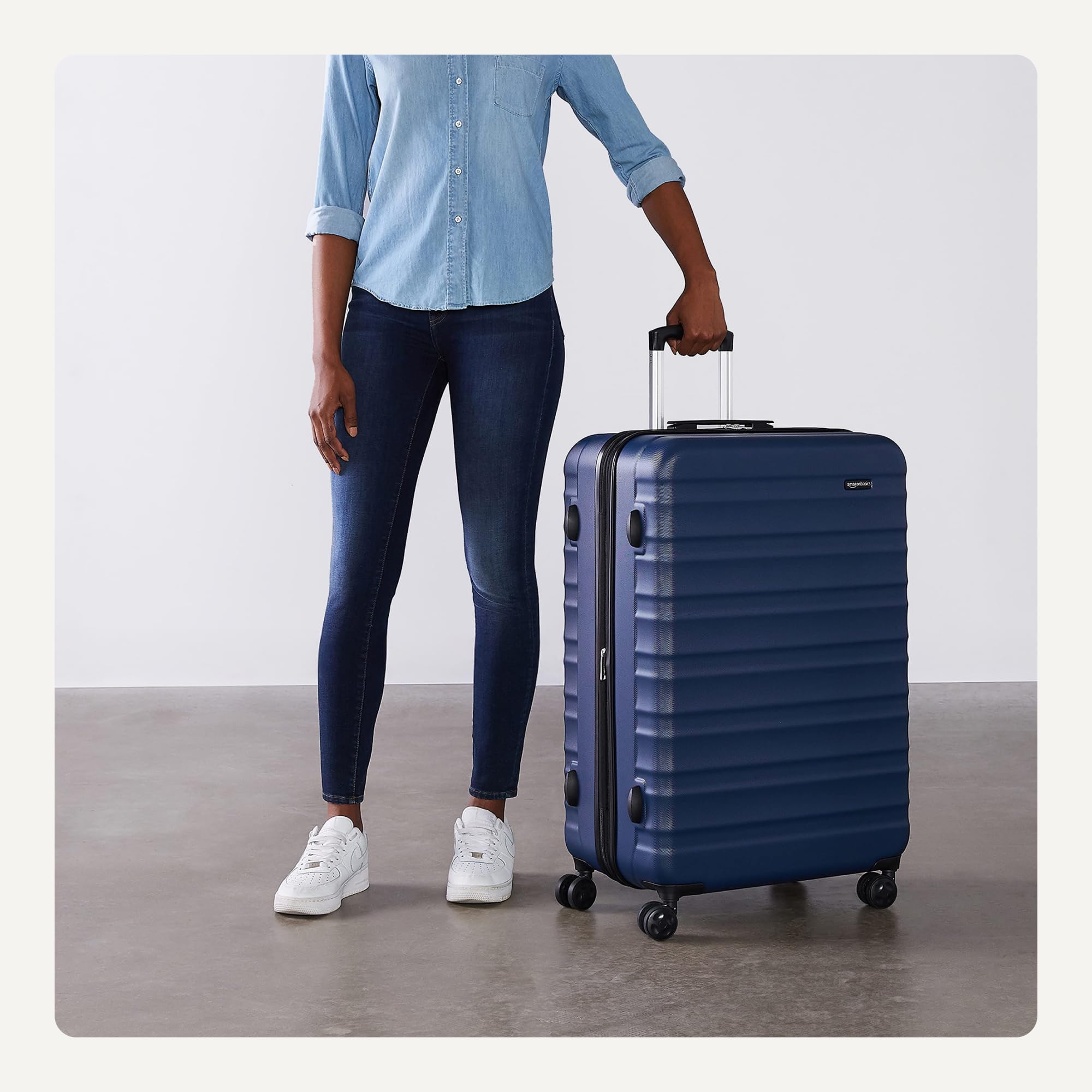 Person standing next to large ABS luggage navy blue with four wheels and telescopic handle