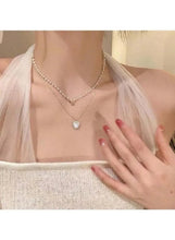 Layered pearl pendant necklace on model, gold-tone chains with pearl beads and small round charm