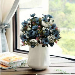 Light blue artificial flower bouquet with peony flowers arranged in a white vase by the window