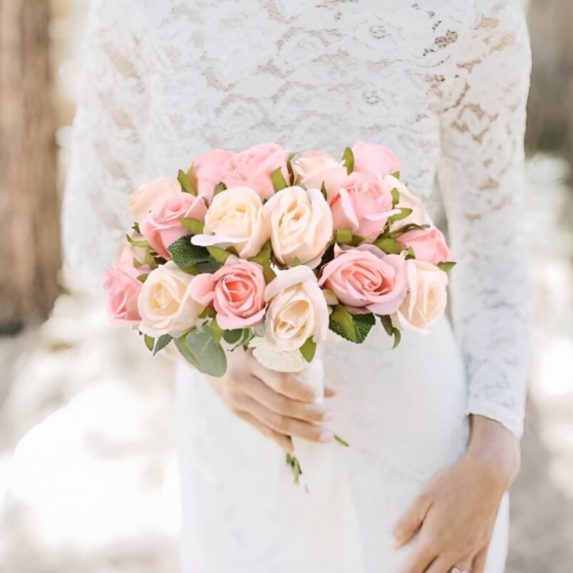 Bride holding light pink faux roses arrangement in a bouquet with green leaves