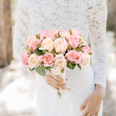Bride holding light pink faux roses arrangement in a bouquet with green leaves