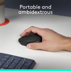 Hand holding Logitech M171 wireless mouse on white desk with keyboard and portable ambidextrous design