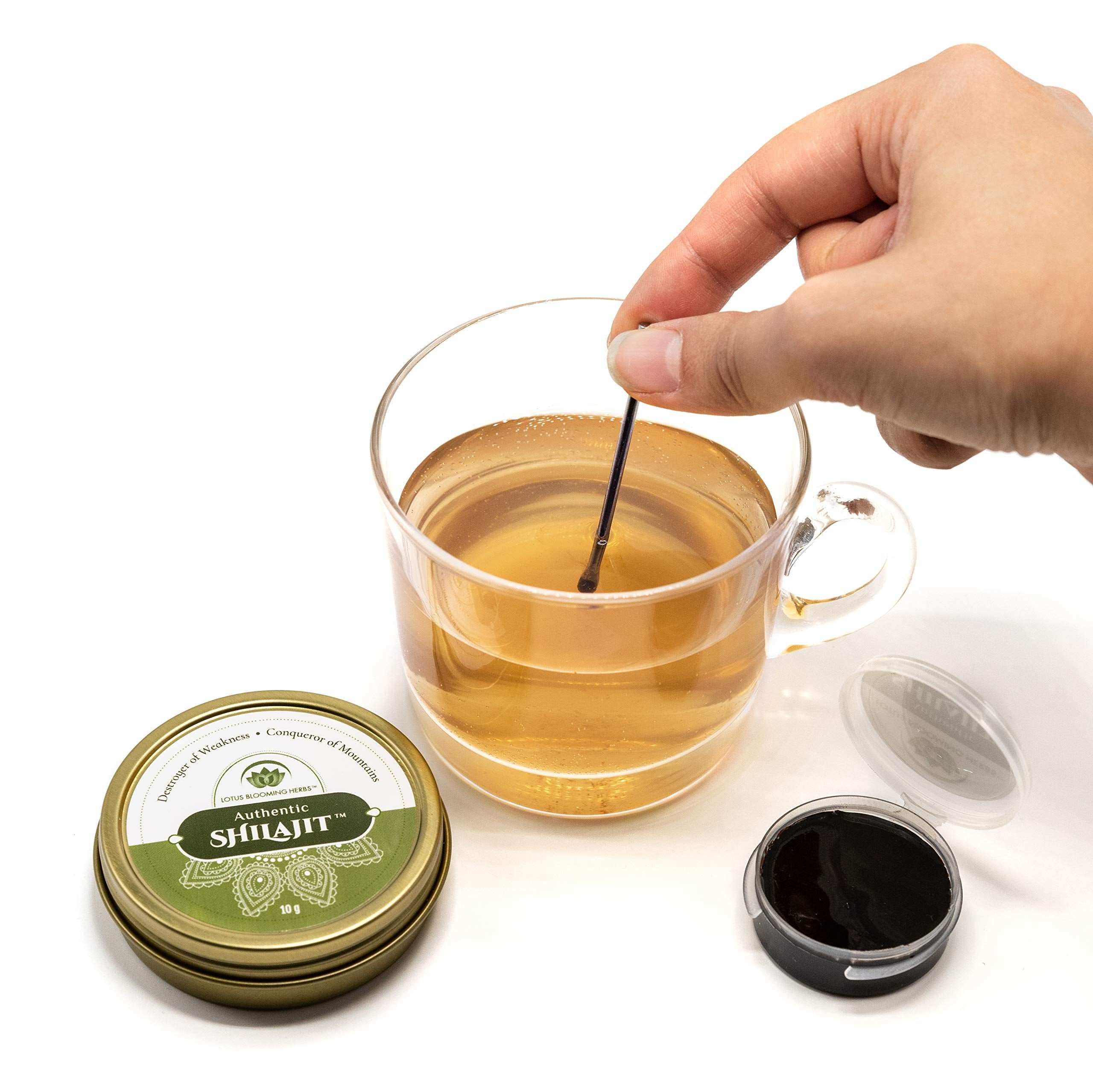 Hand stirring tea beside open tin and jar of pure Himalayan shilajit resin by Lotus Blooming Herbs