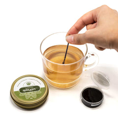 Hand stirring tea beside open tin and jar of pure Himalayan shilajit resin by Lotus Blooming Herbs