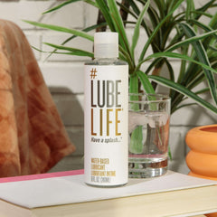 Lube Life bottle of water based personal lubricant on a book next to a glass of water and houseplant