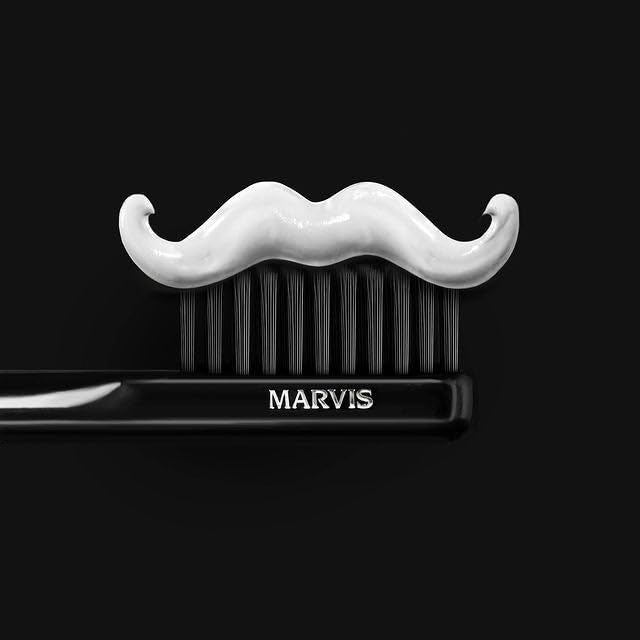 Marvis medium toothbrush black handle with MARVIS logo and white mustache shaped toothpaste on black bristles