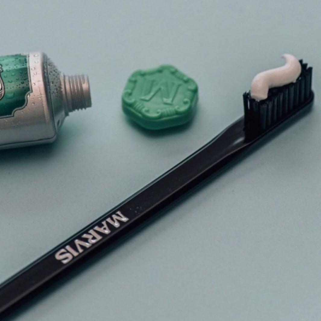 Marvis medium toothbrush with black handle and white paste next to green Marvis toothpaste tube