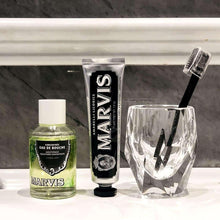 Marvis strong mint mouthwash concentrate bottle, tube, and clear cup with black brush