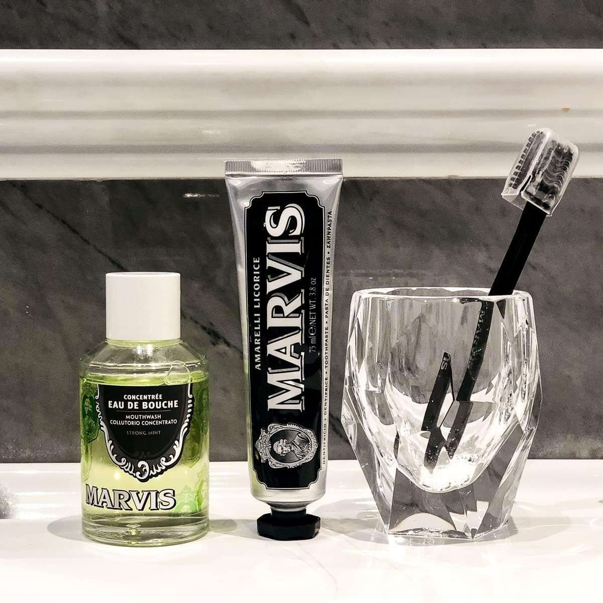 Marvis strong mint mouthwash bottle with Marvis black licorice toothpaste and toothbrush in glass on sink
