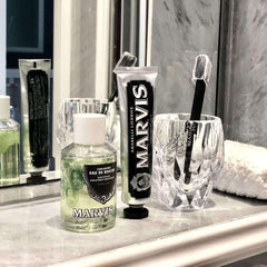 Bottle of Marvis strong mint mouthwash on marble vanity with Marvis toothpaste tube and black toothbrush