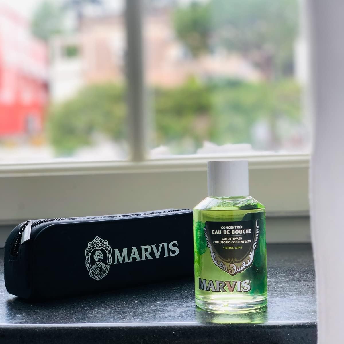 Marvis strong mint mouthwash travel bottle and black Marvis zip pouch on windowsill in natural light