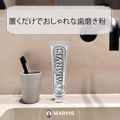 Marvis Whitening Mint Toothpaste tube standing on a beige bathroom sink next to a black toothbrush in cup