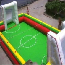 Inflatable football pitch with green turf, red and yellow padded sides, white goal