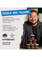 Chef smiling while holding chili crunch jars with stacked small spice bottles