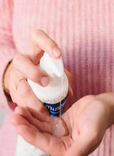 Hands pressing the pump of a Mustela cleansing gel bottle