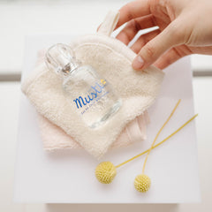 Mustela perfume for babies bottle placed on soft beige towel with hand and decorative yellow flowers