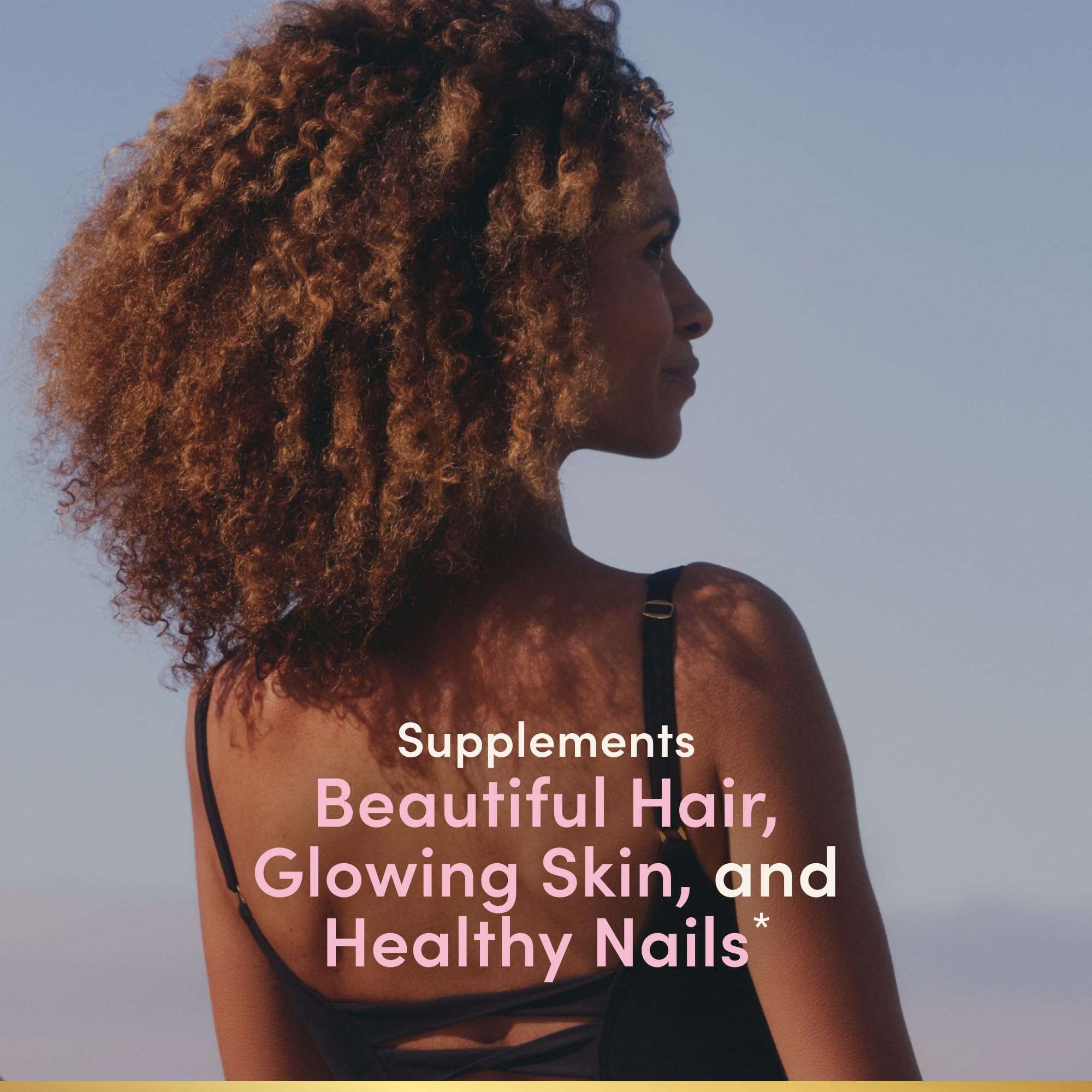 Woman with natural curly hair looking away on beach promoting Nature's Bounty hair supplements for healthy hair and skin