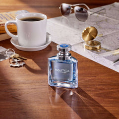 Nautica Voyage long lasting scent cologne bottle on wooden table with coffee cup, map, sunglasses, and compass