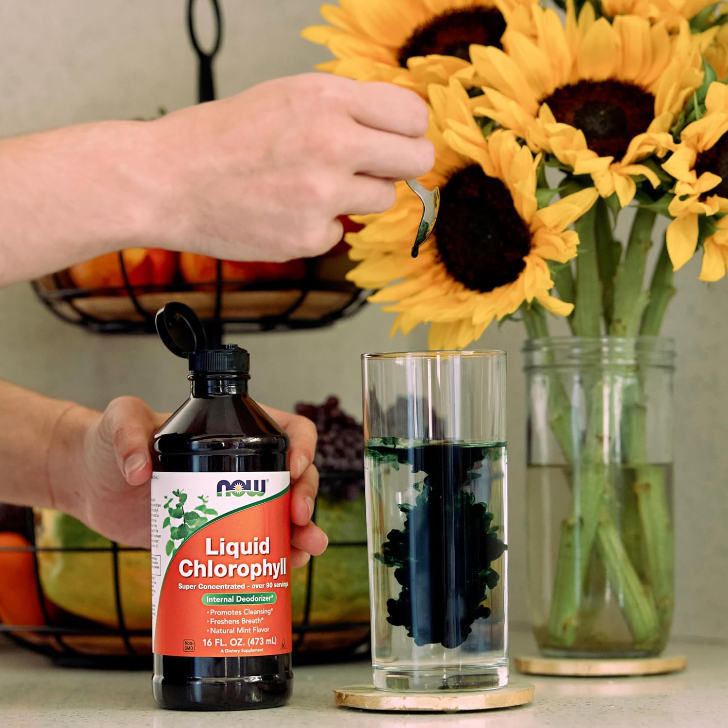 NOW Foods Liquid Chlorophyll Mint Flavor being added to a glass of water with sunflowers in the background