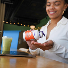 NOW Foods NAC 600 mg supplement in a woman's hand while using a laptop in a cafe
