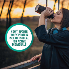 Woman with headphones drinking from shaker outdoors at sunset with NOW Sports branding whey protein isolate powder UAE