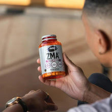 Hand holding NOW Sports ZMA bottle with orange capsule label