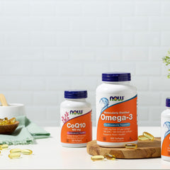 Now Foods Omega-3 softgels bottle with NOW CoQ10 supplement and loose golden softgels on kitchen counter