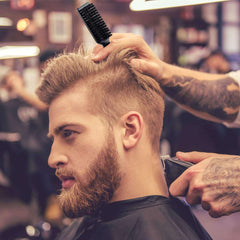 Barber using nylon clipper cleaning brush on a man's haircut in a busy barbershop
