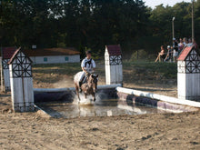 Rider on horseback splashing through water in outdoor arena