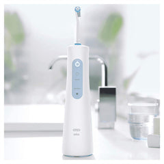 Oral-B Aquacare water flosser white cordless unit on bathroom counter with faucet and glass of water