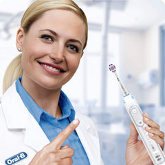 Smiling dentist in white coat pointing to an electric toothbrush fitted with Oral-B 3D White replacement brush heads.
