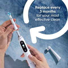 Hands replacing brush head on white electric toothbrush showing Oral-B iO Series replacement brush heads and three month reminder