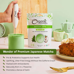 Organic Traditions pouch and frothy cup being whisked with hand frother, slice of cake, organic matcha latte with probiotics