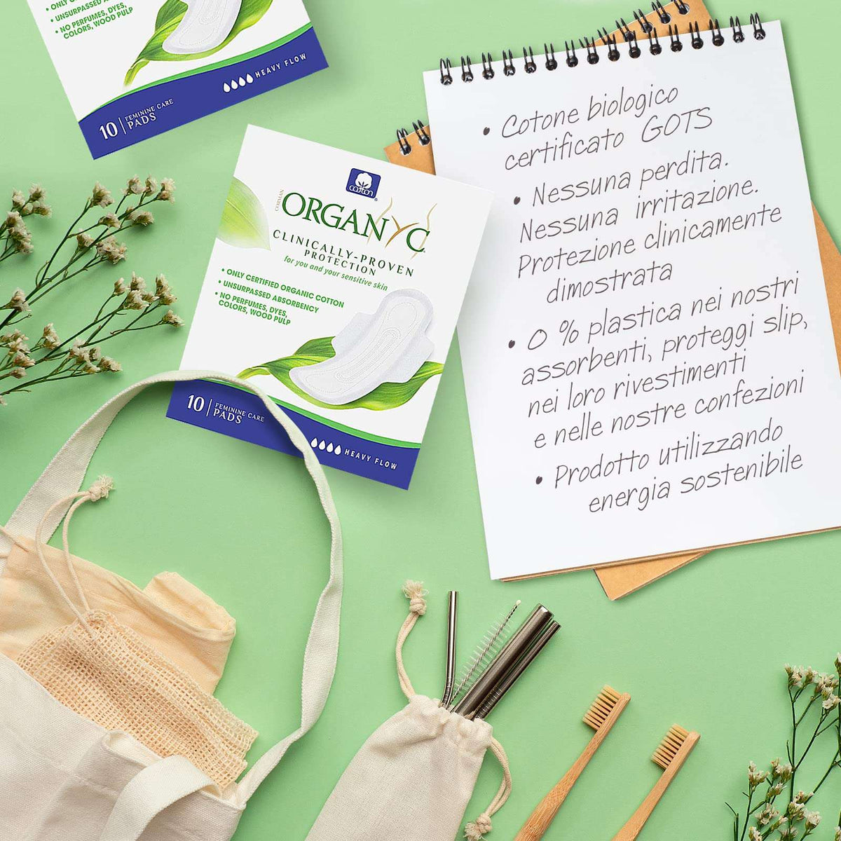 Organyc packaging and cotton sanitary pads on green background with reusable items, organic heavy flow night pads