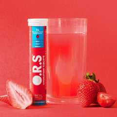 ORS hydration tablets strawberry flavor tube next to glass of pink rehydration drink and fresh strawberries