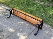Red slatted bench with black metal frame and arched end legs on stone pavers