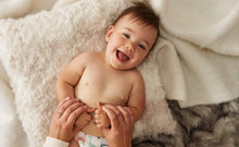 Smiling infant resting on blanket, hands near mouth