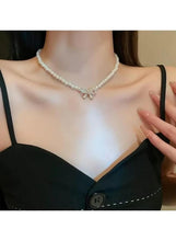 Pearl necklace with bow pendant and rhinestone details, close-up on neckline