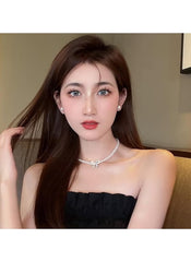 Huitich pearl necklace with bow pendant worn by woman with long brown hair and black strapless top