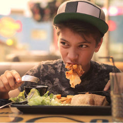 Young person eating pizza using fork from 12 piece cutlery set while dining at restaurant