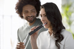 Woman brushing with black Philips Sonicare 4100 electric toothbrush UAE in bright bathroom with smiling partner