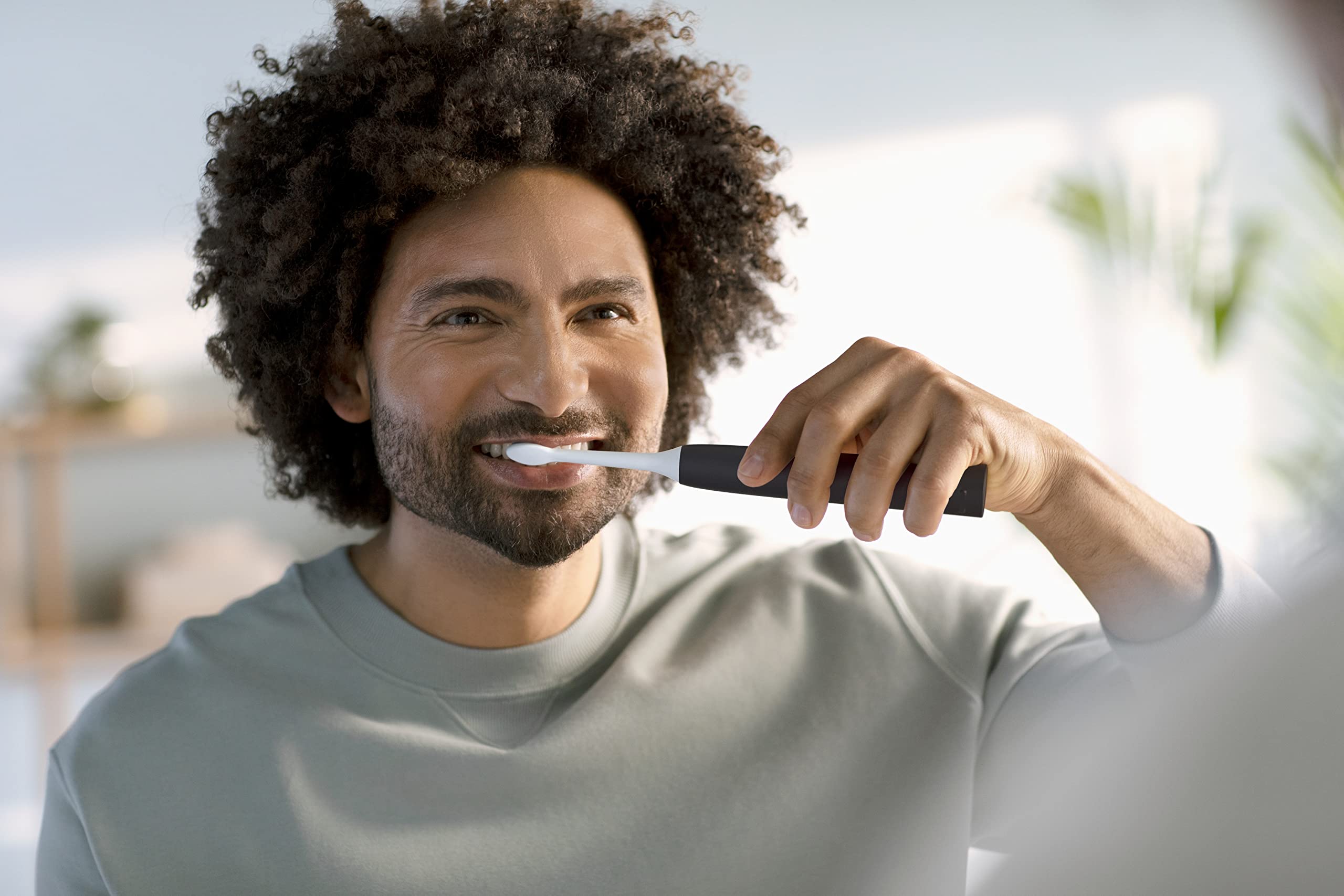 Man brushing teeth with Philips Sonicare 4100 electric toothbrush UAE in bathroom mirror smiling during morning routine